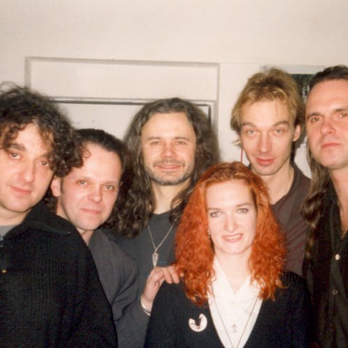 Die Band posiert hinter der Bühne für ein Foto. Vorn rechts eine junge Frau.